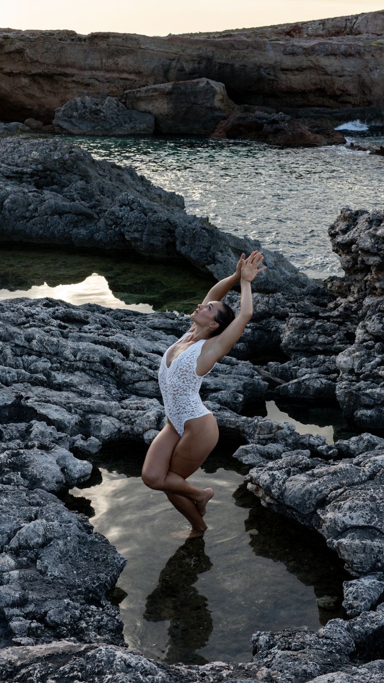 Anita dancing in a rock pool by the sea, arms reaching up